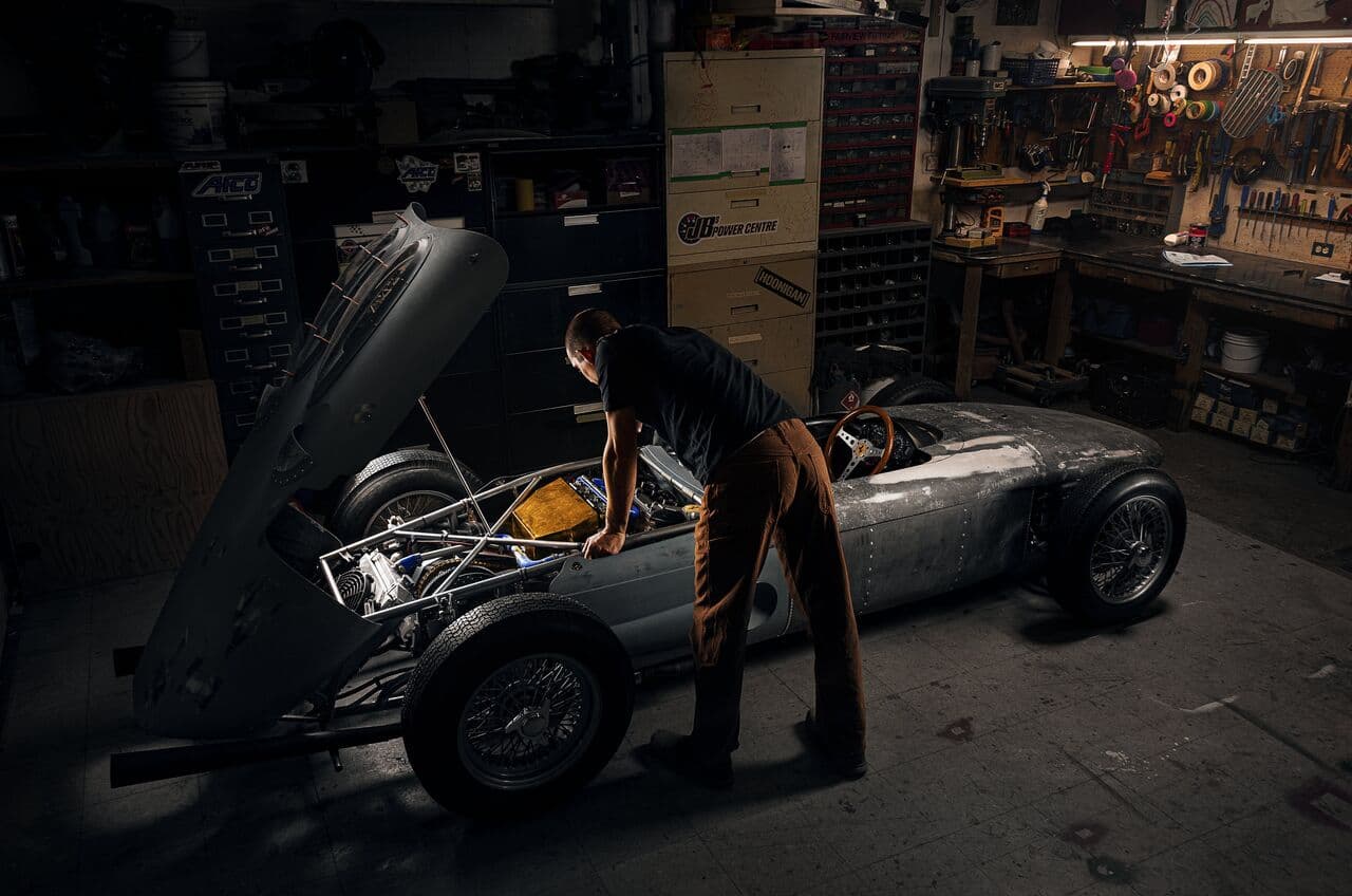 A mechanic leaning into the engine bay of a classic racing car in a workshop