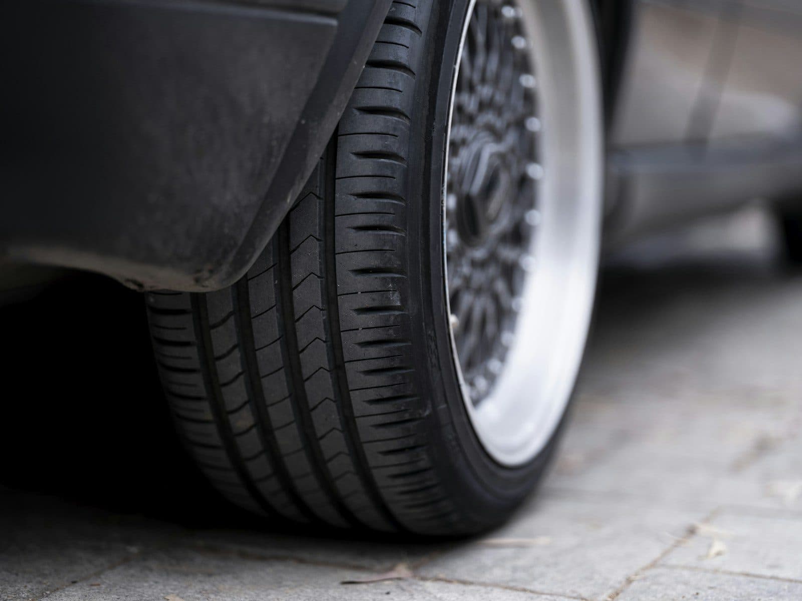A close-up of a car tyre and mesh alloy wheel parked on block paving