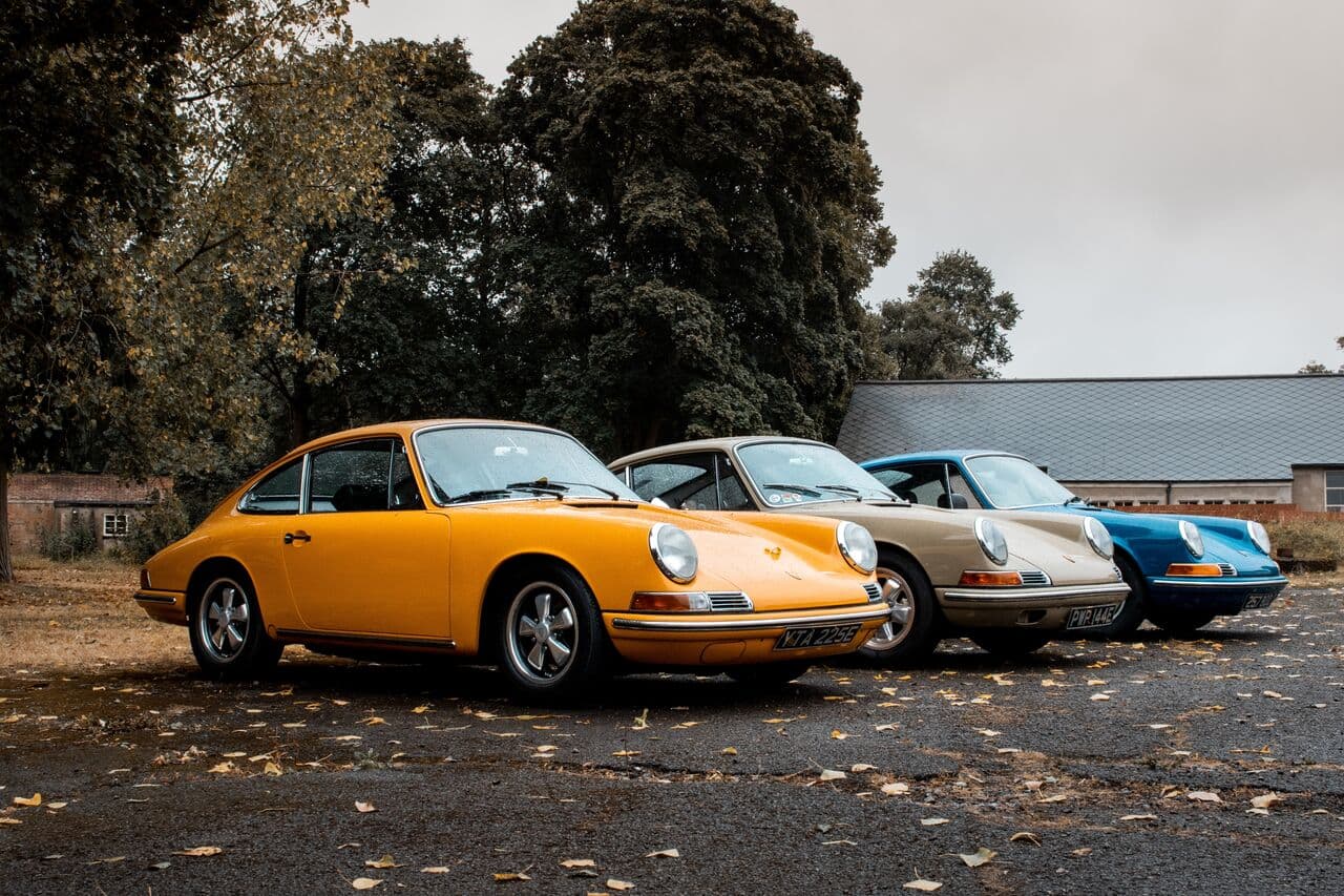 Three classic Porsche 911s parked on a yard scattered with autumn leaves