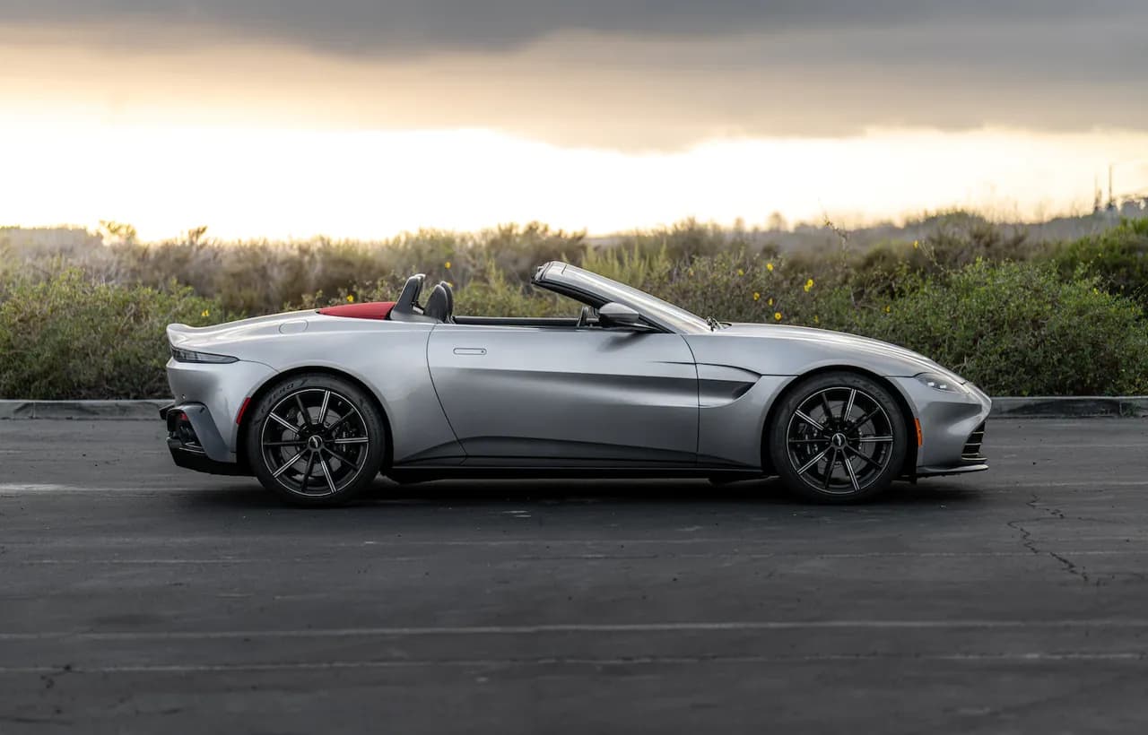 A silver convertible sports car with its roof folded down, parked at dusk