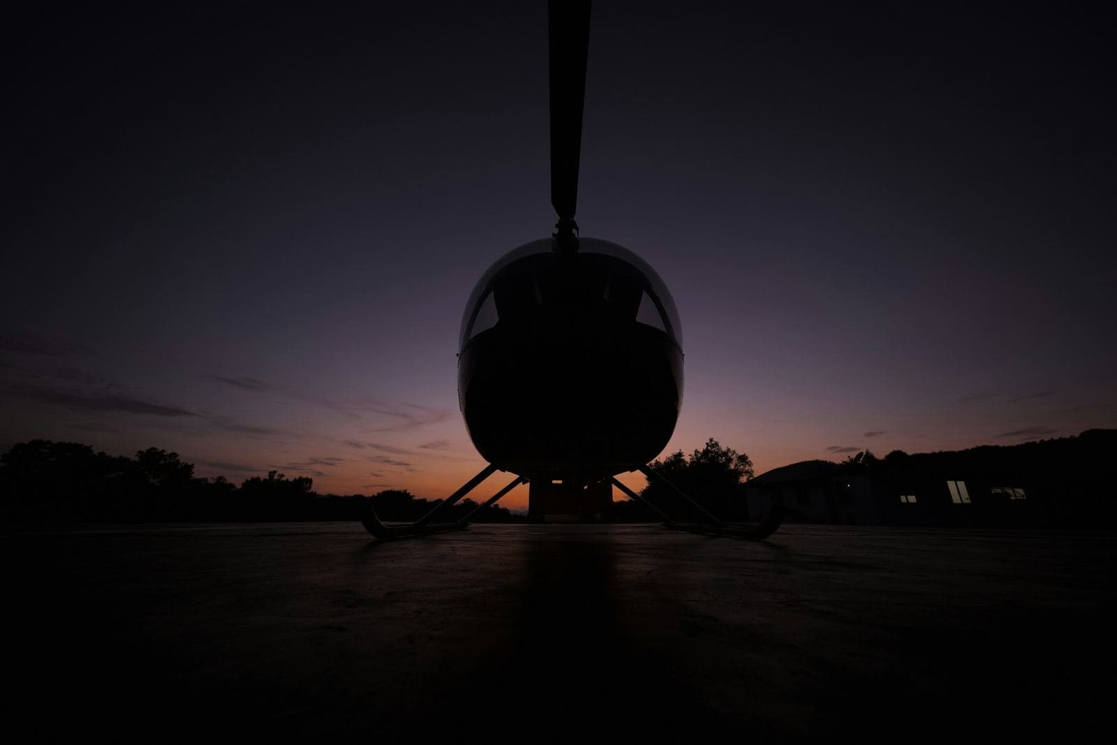 A small helicopter silhouetted on a landing pad at dusk