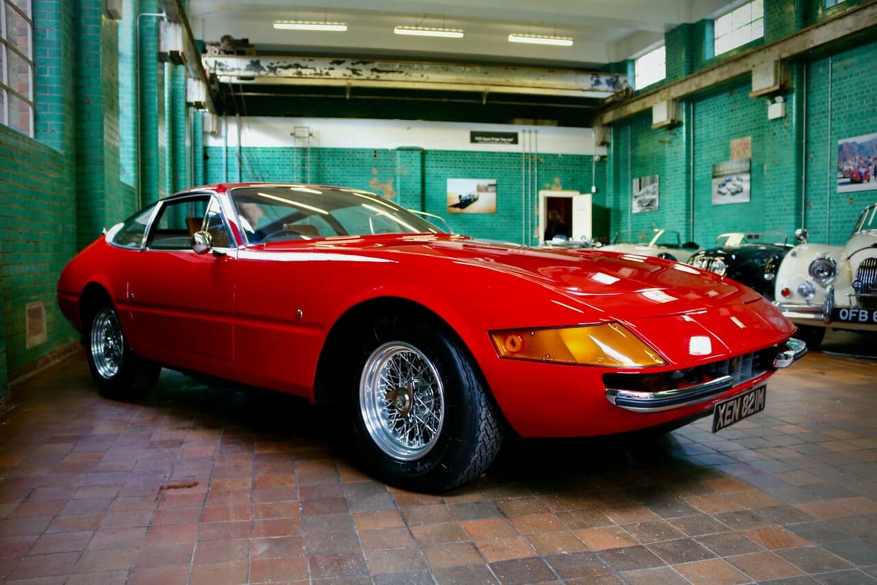 A red classic Ferrari parked indoors beside other classic cars